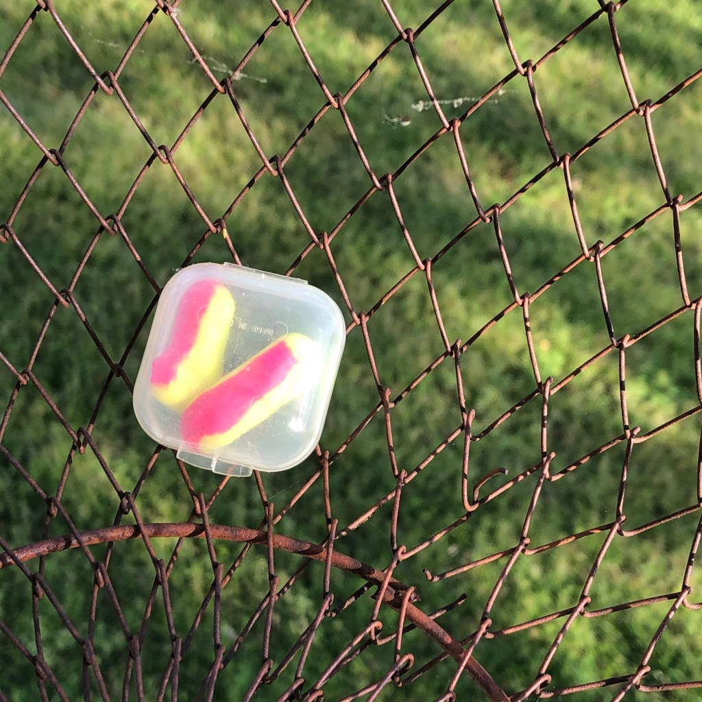 Picture of two yellow and pink earplugs in a small clear plastic travel container.