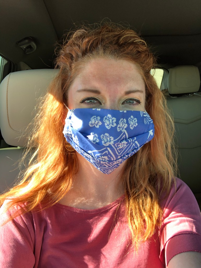 Red-haired girl in a pink shirt wearing a white a blue floral patterned face mask.